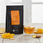 Pouch Chá Apfeltraum Moncloa ao lado de xícara com chá quente e frutas tropicais