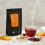 Pouch Chá Orange Sky Moncloa ao lado de xícara com chá quente de hibisco e laranja